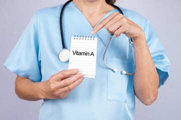 Ärztin mit Stethoskop zeigt auf einen kleinen Notizblock auf dem Vitamin A steht