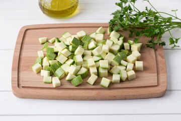 Wooden board with diced zucchini, a bunch of parsley and olive oil on a white background. Cooking delicious vegan food