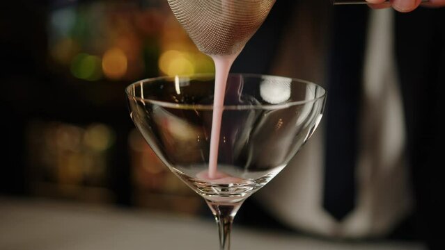 The bartender pours a cocktail through a strainer whipped pink cocktail. Sweet alcohol cocktail at the bar