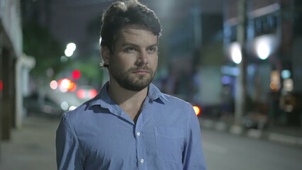 Pensive young man walking in city street at night. Thoughtful person walks in urban sidewalk in mental reflection in the evening