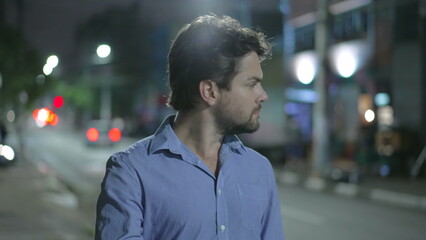 Pensive young man walking in city street at night. Thoughtful person walks in urban sidewalk in mental reflection in the evening