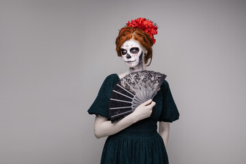 Elegant scary halloween costume. Mexican Day of the Dead Tradition. Skull with flowers makeup for a party. Party ideas. Mysterious portrait of a woman with a painted face. scary face. grey background