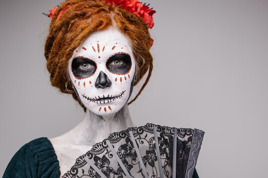 Elegant scary halloween costume. Mexican Day of the Dead Tradition. Skull with flowers makeup for a party. Party ideas. Mysterious portrait of a woman with a painted face. scary face. grey background