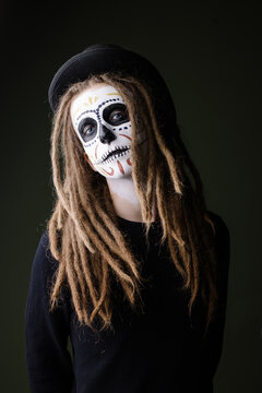 Portrait of a man in a skull suit. Traditional makeup for day of the dead mexico. Modern hipster with dreadlocks men's halloween makeup idea. carnival costume skeleton party. Dark mystery background 