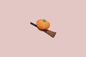 Candy sugar orange pumpkin on a witch broom stick on pink background with copy space. Minimal halloween holiday celebration horror concept. Autumn party idea.