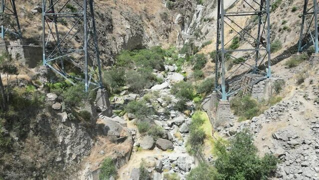 Aerial dolly drone shot through a railroad bridge in the mountains of matacuna lima in peru with view of the steel girders, plants and rocks on a sunny day