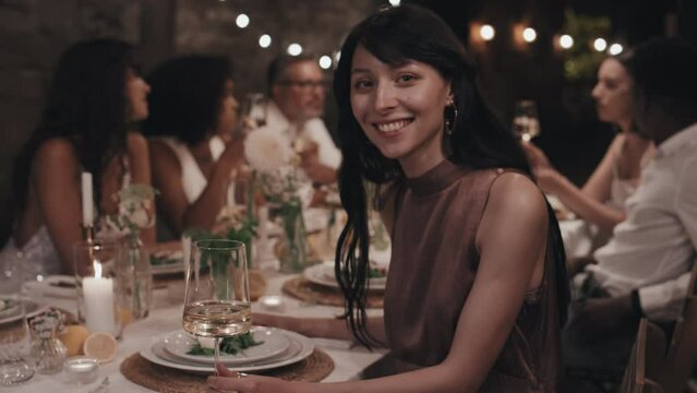 Selective focus of modern young Caucasian woman with ling hair wearing elegant clothes sitting dining table at wedding party smiling at camera