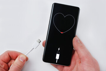 Holds charging cable and smartphone showing low battery in heart shape