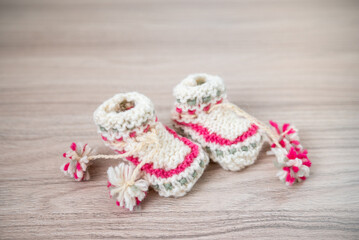 Knitted children socks on a wooden table. Handmade wollen socks. Warm winter clothes for baby. Cute pink and yellow baby socks. Child fashion. Knitted baby boots