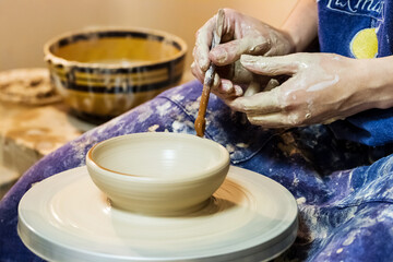 Female hand working on pottery wheel and draw a pattern on a clay plate