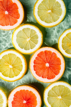 Vertical colorful background image of fruit citrus lemon, orange, grapefruit, slices in water splashing fresh transparent surface with flecks. Flat lay, top view. Summer beach tropical