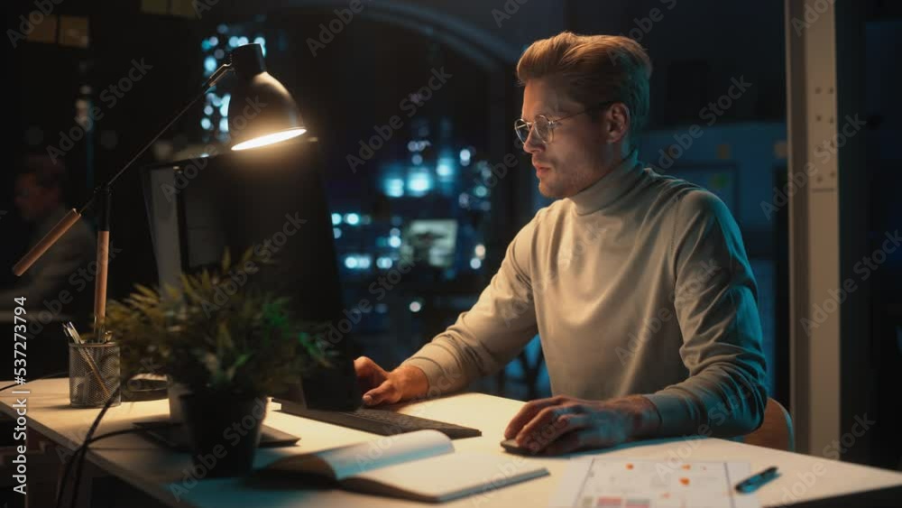 Poster Handsome Man Working on Desktop Computer in a Company Office at Night. Young Specialist Analyzing Reports. Marketing Assistant Developing a Consumer Sales Strategy for a Client.