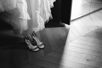 scarpa di matrimonio, vicino al vestito da sposa, dentro ad una camera con pavimento in legno....