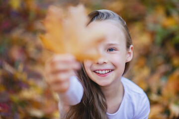 A beautiful girl is holding a maple leaf in front of her.
