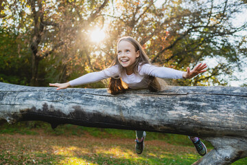 A cute girl lies on a log stretched arms like airplane wings