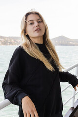Obraz premium young blonde woman in black sweater looking at camera from ferry boat crossing bosporus in istanbul.