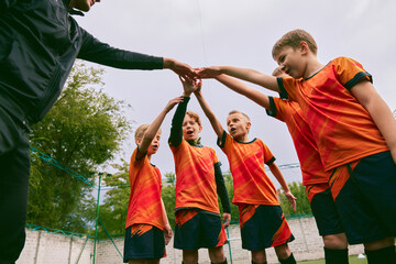 Determined to win. Junior soccer team stacking hands before a match, outdoors. Concept of sport, competition, studying and achievements