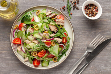 Fresh salad with vegetables and fish. Arugula, spinach, cucumbers, tomato, onions and fish in a plate on the table. Diet nutrition. Top view. Copy space