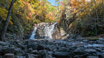 Beautiful forty-foot tall, fifty-foot-wide waterfall framed by colorful autumn foliage and river stones.
