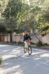 young blonde woman in trendy outfit riding bicycle on sunny street in turkey.