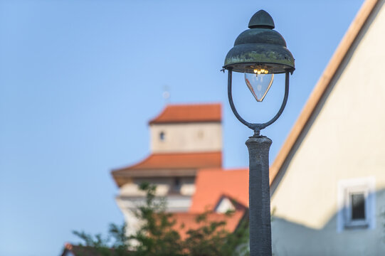 Modernisierte historische Gaslaterne vor mittelalterlichem Turm Reimlinger Tor an umlaufender Stadtmauer mit &uuml;berdachtem Wehrgang in N&ouml;rdlingen vor blauem Himmel.