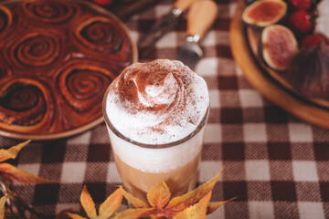 Pumpkin spice whipped latte in glass. Hot autumn drink beverage. Nearby delicious pie and appetizers fruits and cheese.