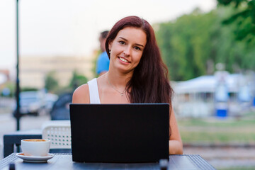 Smiling sensuality caucasian business woman with brunette hair working on laptop in outdoor cafe. College student using technology ,online education, freelance.Summer day.