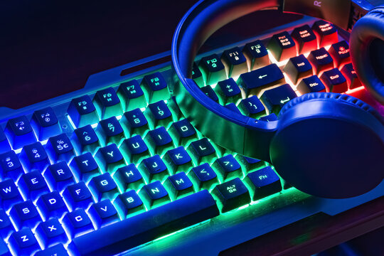 Pro gaming illuminated desk, headset, keyboard, computer neon lights. Cyber sport equipment laying on desktop, ready for online video gaming.Dark shot.