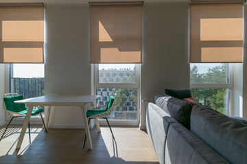 Roller blinds in the interior. Roller shades automatic on large windows to the floor in the interior. Armchairs with green pillows in the kitchen near windows with motorized roller blinds. Sunny day.  - Powered by Adobe
