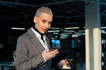 Pensive young woman with short hair uses mobile phone in office.