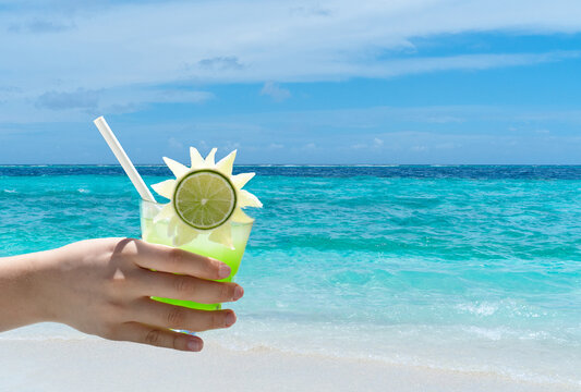 Female Holding Glass Of Bright Green Cocktail On The Beach