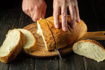 Whole grain bread put on kitchen wood board with a chef holding knife for cut. Fresh bread on table...
