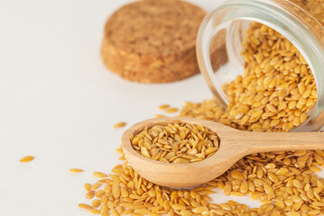 Macro photo of raw golden flax seeds in glass scattered on the table with a wooden spoon, composition with organic food