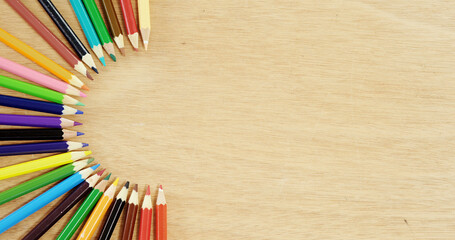 Obraz premium Overhead view of multicolored pencils arranged on wooden table, copy space