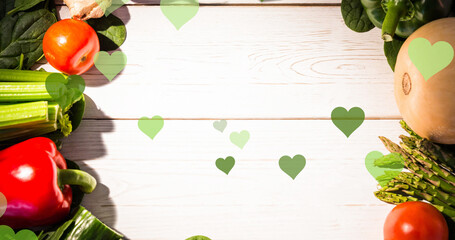 Composite of green heart shapes over various fresh vegetables on wooden table, copy space
