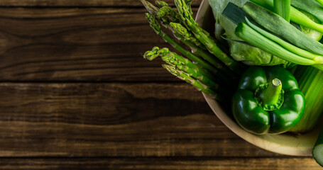 Close-up of fresh asparagus, green bell pepper, cucumber, chinese cabbage in bowl on wooden table