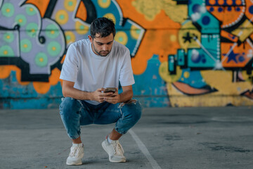 urban young man with mobile phone in the street outdoors with graffiti on the wall