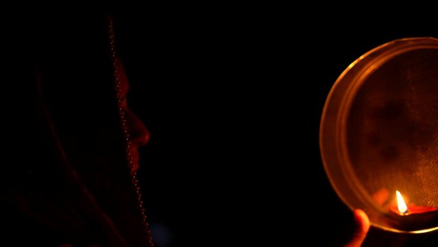 Woman hand holding Karwa Chauth strainer for the Karwa Chauth celebration on the night. Karwa Chauth strainer and Diya oil lamps for the Karwa Chauth celebration on the night