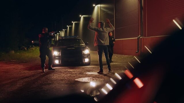 Two Police Officers Aim Gub at Suspect, Order Him to Get on the Knees and Hands Back, Arrest and Cuff Felon. Officers of the Law Handcuff Dangerous Criminal on Dark City Street. Cinematic Shot