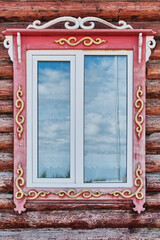 Window with carved wooden architraves and gold color pattern on log facade, Buryatia, Russia.