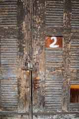 Old wooden door with hand painted number two, 2, closed with padlock, partial view, background