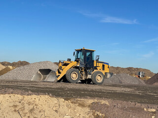 Excavator Machine at Excavation Earthmoving Work in Sand Quarry. Excavator against Blue Sky. Heavy Machine Construction Site
