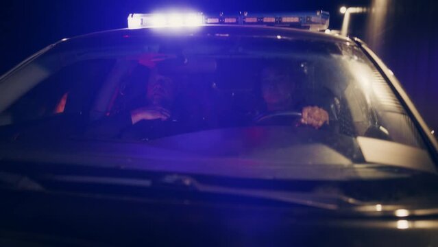 Point of View: Night Shift Two Police Officers on Duty Driving Traffic Patrol Car, Siren Blasts Flashligh and Start Chasing a Suspect. Squad Car Cops in Pursuit of Criminal. Cinematic Night Shot
