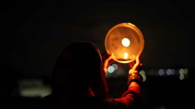 Woman hand holding Karwa Chauth strainer for the Karwa Chauth celebration on the night. Karwa Chauth strainer and Diya oil lamps for the Karwa Chauth celebration on the night