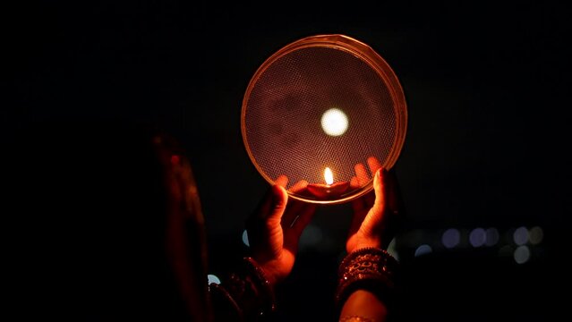Woman hand holding Karwa Chauth strainer for the Karwa Chauth celebration on the night. Karwa Chauth strainer and Diya oil lamps for the Karwa Chauth celebration on the night