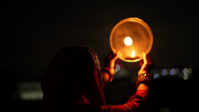 Woman hand holding Karwa Chauth strainer for the Karwa Chauth celebration on the night. Karwa Chauth strainer and Diya oil lamps for the Karwa Chauth celebration on the night
