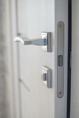 Close-up of apartment interior elements. Open gray door. Chromed door handle and lock with key.