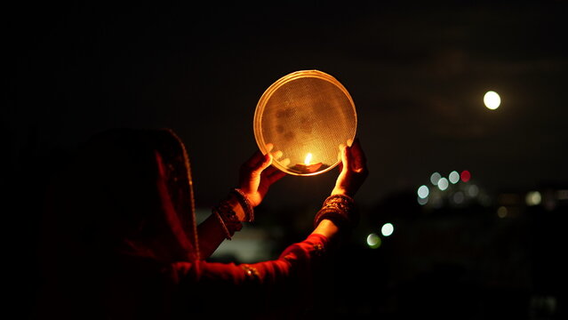 Woman hand holding Karwa Chauth strainer for the Karwa Chauth celebration on the night. Karwa Chauth strainer and Diya oil lamps for the Karwa Chauth celebration on the night