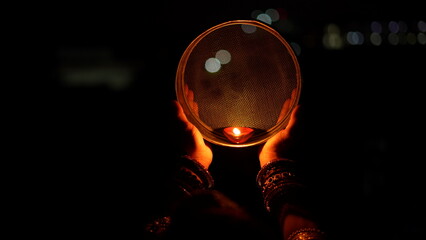 Woman hand holding Karwa Chauth strainer for the Karwa Chauth celebration on the night. Karwa Chauth strainer and Diya oil lamps for the Karwa Chauth celebration on the night