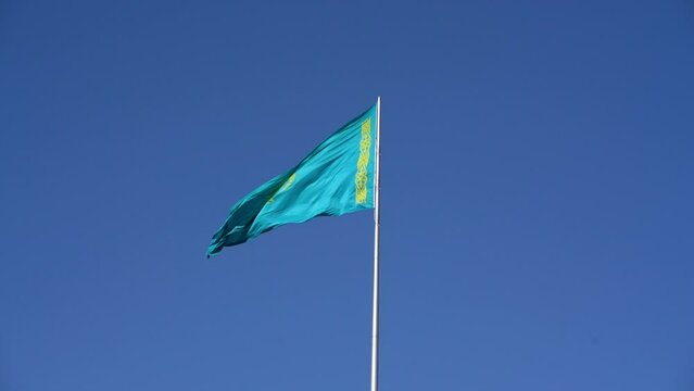 The flag of Kazakhstan is flying against a cloudless blue sky. Banner for the site, covers.